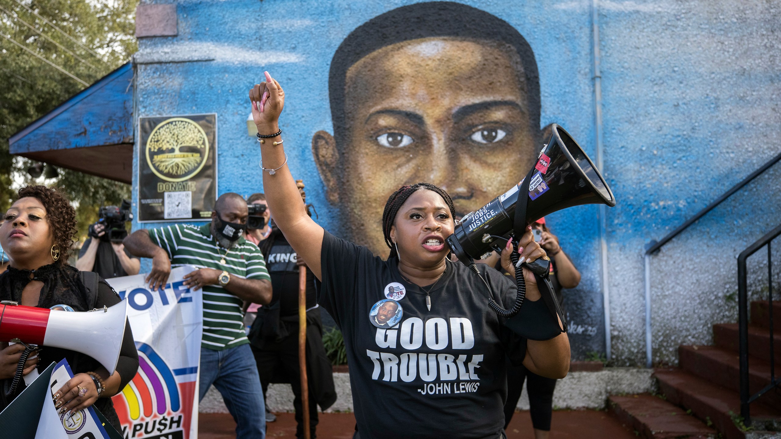 FILE - Civil rights activist Porchse Miller, of Atlanta, shouts into a megaphone in front of a mural of Ahmaud Arbery during march that followed the Wall of Prayer event outside the Glynn County Courthouse, Nov. 18, 2021, in Brunswick, Ga. (AP Photo/Stephen B. Morton, File)