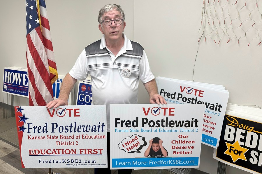 Fred Postlewait, a Republican candidate for the Kansas State Board of Education from Kansas City, Kan., shows off two of the yard signs available for supporters at the Republican Party's local headquarters in Johnson County, Tuesday, Oct. 1, 2024, in Overland Park, Kan. (AP Photo/John Hanna)