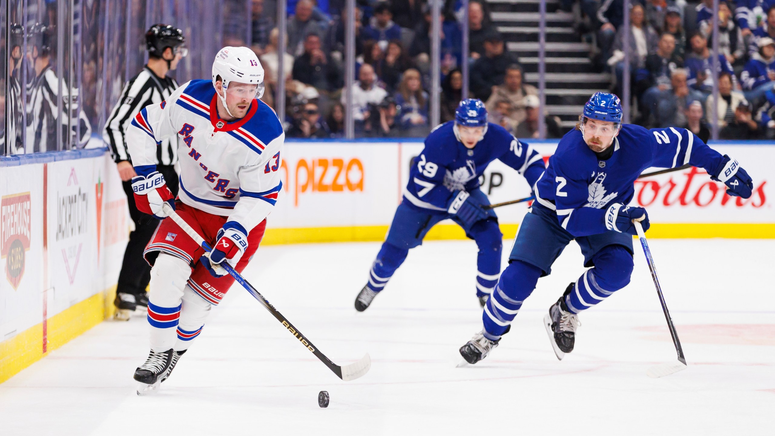 New York Rangers left wing Alexis Lafreniere (13) skates the puck up ice as he's trailed by Toronto Maple Leafs defenceman Simon Benoit (2) during first period NHL hockey action in Toronto on Saturday, October 19, 2024. (Cole Burston/The Canadian Press via AP)