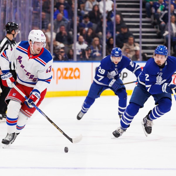 New York Rangers left wing Alexis Lafreniere (13) skates the puck up ice as he's trailed by Toronto Maple Leafs defenceman Simon Benoit (2) during first period NHL hockey action in Toronto on Saturday, October 19, 2024. (Cole Burston/The Canadian Press via AP)