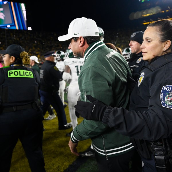 A Michigan State University policewoman holds back head coach Jonathan Smith from getting in the middle of a fight that broke out against Michigan following an NCAA college football game, Saturday, Oct. 26, 2024, in Ann Arbor, Mich. (AP Photo/Jose Juarez)