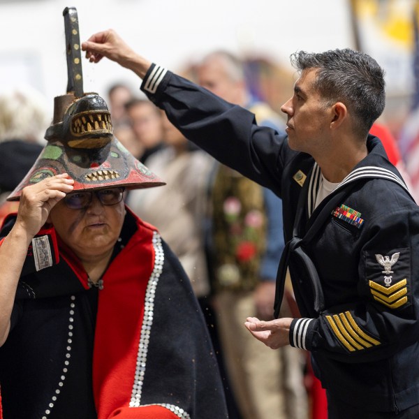 A member of the U.S. Navy sprinkles tobacco on top of a killer whale clan hat, which is considered to bring good fortune, during a Navy ceremony Saturday, Oct. 26, 2024, in Angoon, Alaska, to apologize for the 1882 military bombing of the Tlingit village in Angoon. (Nobu Koch/Sealaska Heritage Institute via AP)