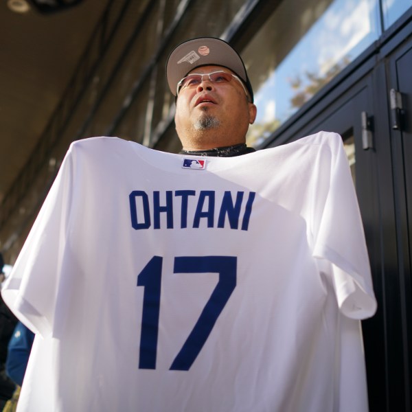 A man shows off a baseball jersey of Shohei Ohtani of the Los Angeles Dodgers as he and others wait in line to watch a live stream of Game 3 of the baseball World Series between the Dodgers and the New York Yankees, in a public viewing event in Oshu, northeastern Japan, the hometown of Ohtani, Tuesday, Oct. 29, 2024. (AP Photo/Eugene Hoshiko)