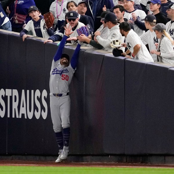 Fans interfere with a foul ball caught by Los Angeles Dodgers right fielder Mookie Betts during the first inning in Game 4 of the baseball World Series against the New York Yankees, Tuesday, Oct. 29, 2024, in New York. (AP Photo/Ashley Landis)