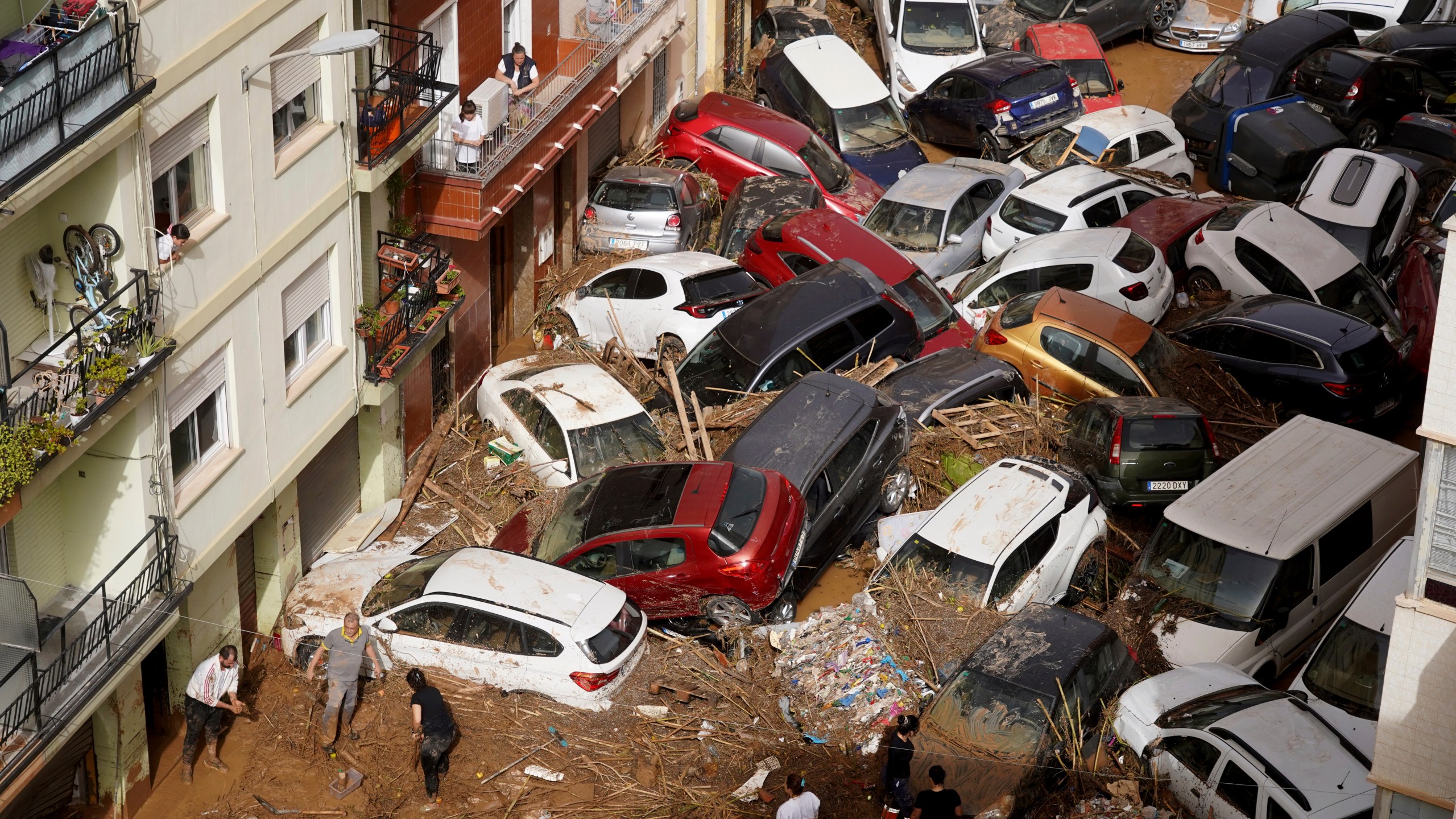 Residents clean the street next to cars piled up after being swept away by floods in Valencia, Spain, Wednesday, Oct. 30, 2024. (AP Photo/Alberto Saiz)