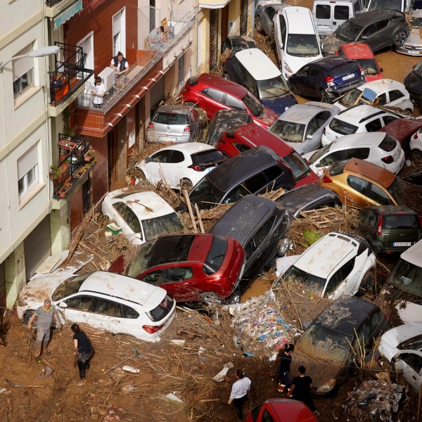 Residents clean the street next to cars piled up after being swept away by floods in Valencia, Spain, Wednesday, Oct. 30, 2024. (AP Photo/Alberto Saiz)