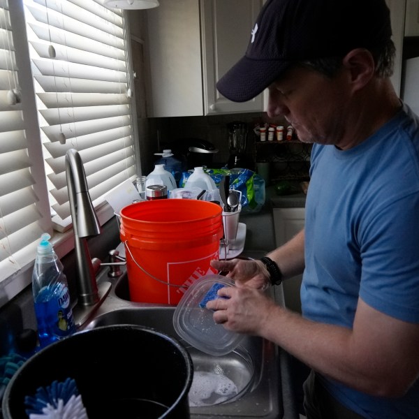 FILE - Travis Edwards captures excess water while cleaning dishes on Oct. 3, 2024, in Asheville, N.C. (AP Photo/Brittany Peterson, File)