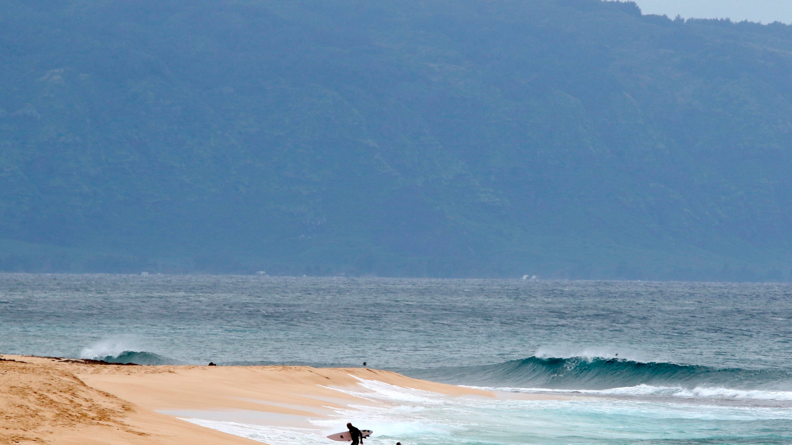 FILE - A surfer walks out of the ocean on Oahu's North Shore near Haleiwa, Hawaii, March 31, 2020. (AP Photo/Caleb Jones, File)