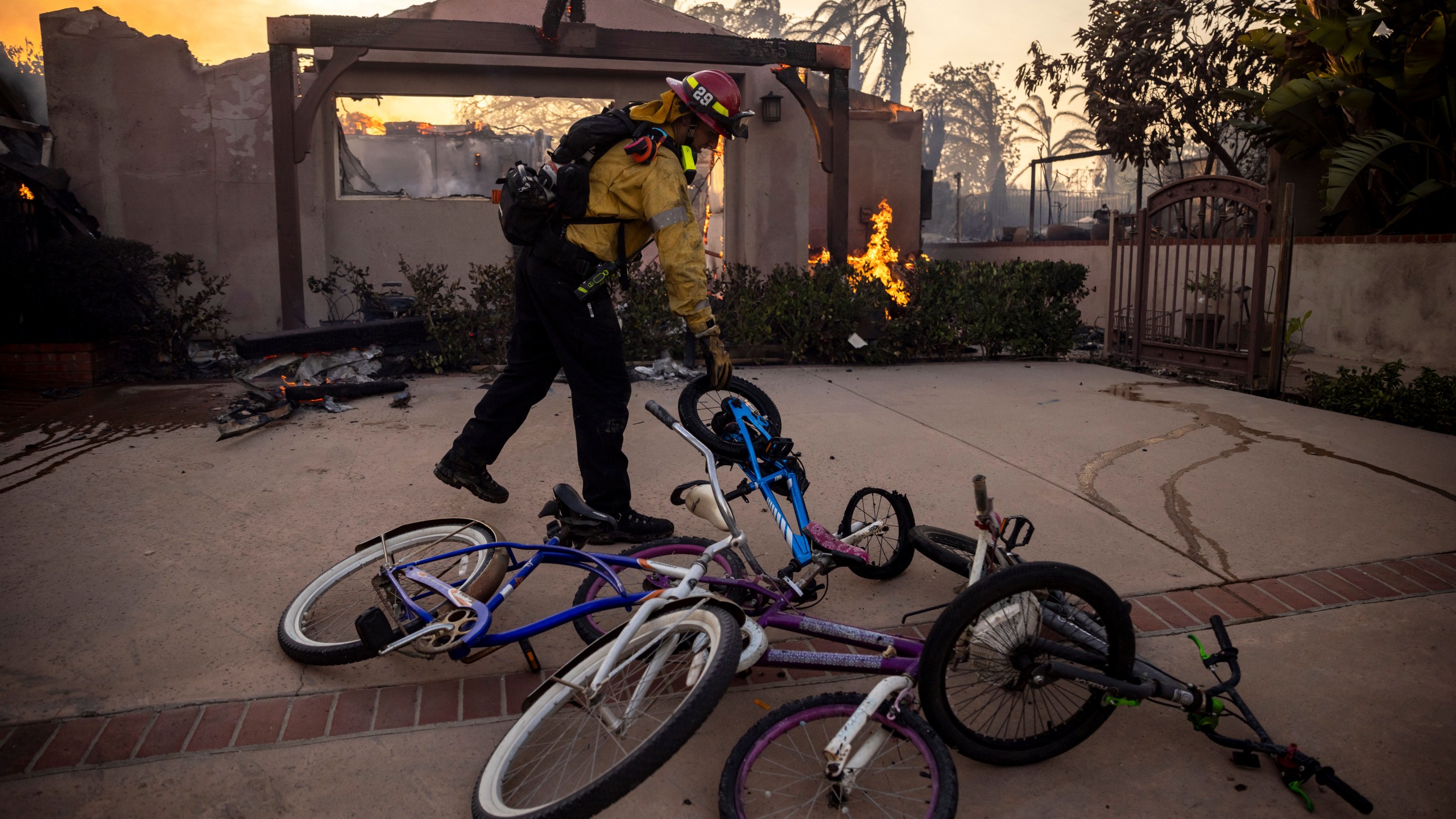 A firefighter, moves bicycles as he works against the Mountain fire, Wednesday, Nov. 6, 2024, near Camarillo, Calif. (AP Photo/Ethan Swope)