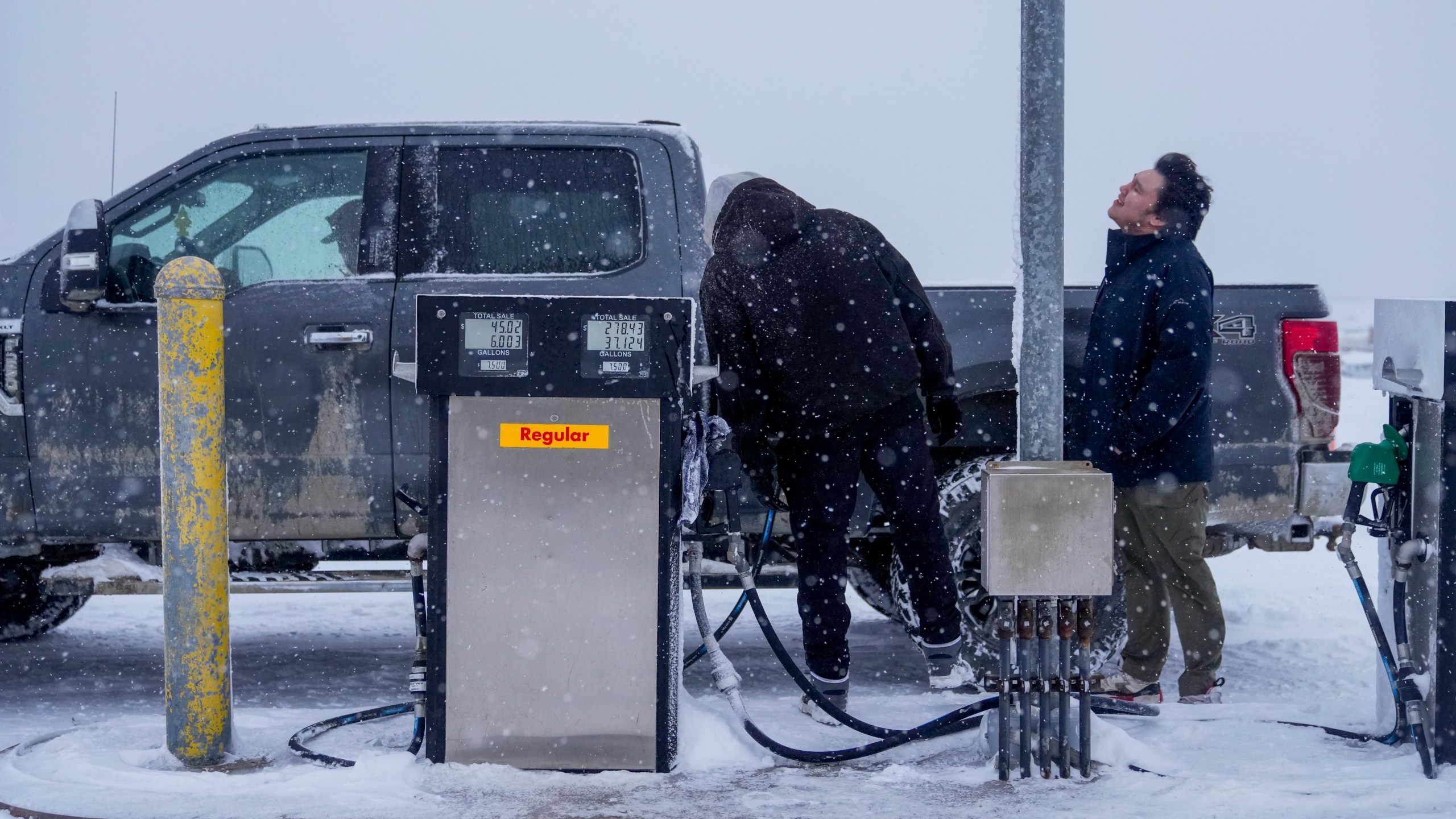 FILE- Edwin Solomon, 18, at right, stands in the wind and snow while filling up a truck with regular gas at a price of $7.50 a gallon, Wednesday, Oct. 16, 2024, in Kaktovik, Alaska. (AP Photo/Lindsey Wasson, File)