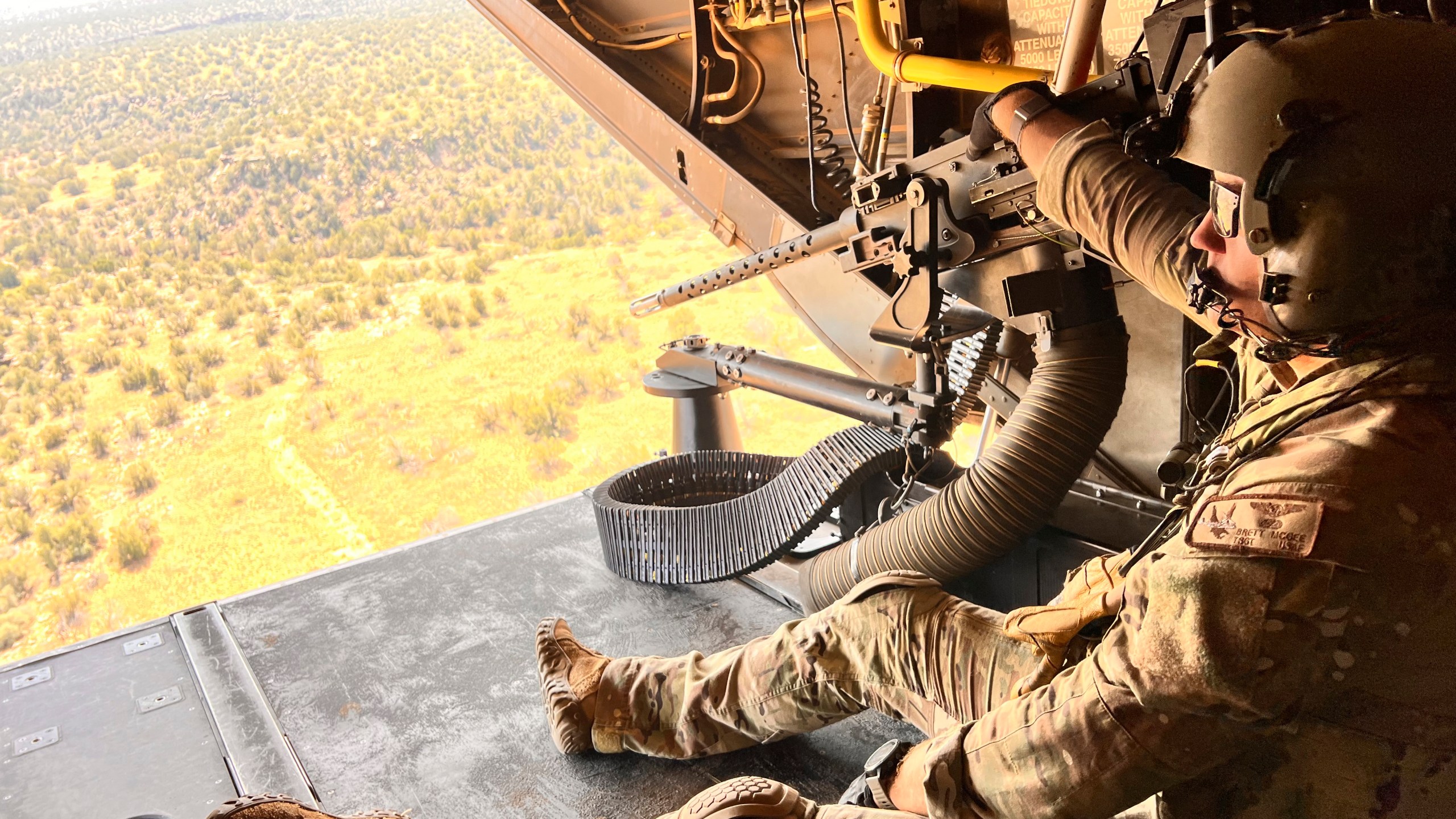 Osprey flight engineer Tech Sgt. Brett McGee sits on the back open ramp of the V-22 and holds the aircraft's .50 caliber gun as the crew flies over a New Mexico training range Oct. 9, 2024, near Cannon Air Force Base. (AP Photo/Tara Copp)