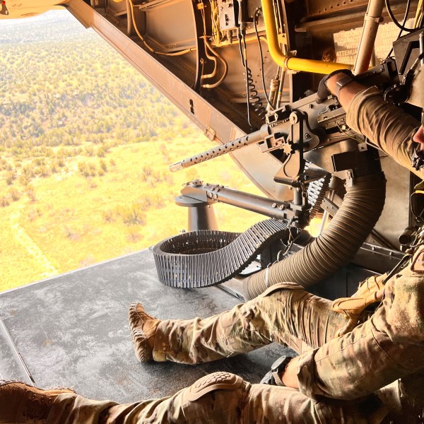 Osprey flight engineer Tech Sgt. Brett McGee sits on the back open ramp of the V-22 and holds the aircraft's .50 caliber gun as the crew flies over a New Mexico training range Oct. 9, 2024, near Cannon Air Force Base. (AP Photo/Tara Copp)