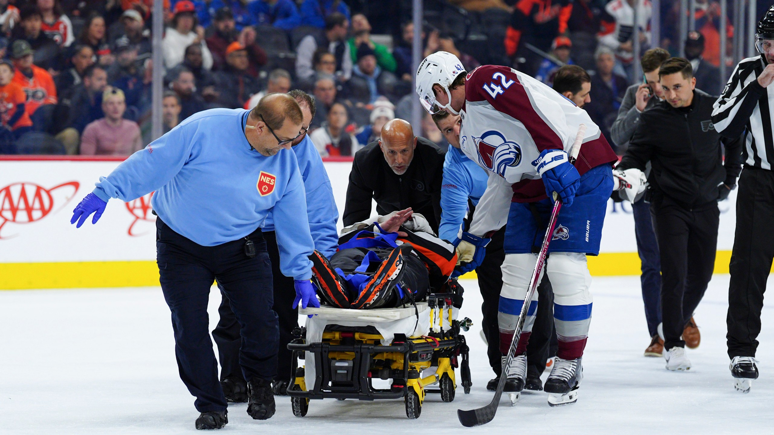 Colorado Avalanche's Josh Manson (42), right, talks to referee Mitch Dunning, center, as Dunning is stretchered off the ice after an injury during the first period of an NHL hockey game between the Philadelphia Flyers and the Avalanche, Monday, Nov. 18, 2024, in Philadelphia. (AP Photo/Derik Hamilton)