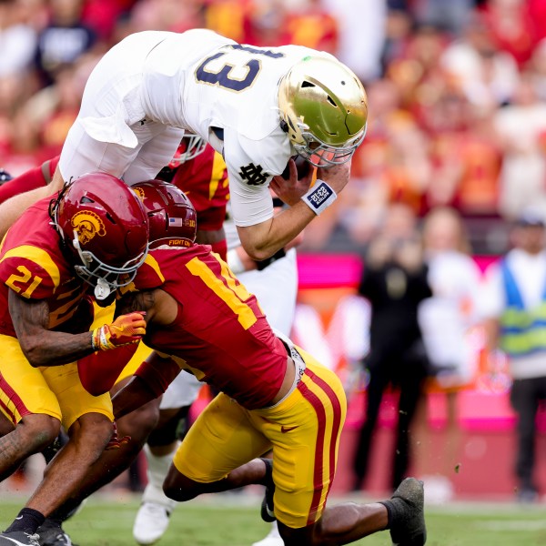 Notre Dame quarterback Riley Leonard, top, dives over Southern California cornerback Greedy Vance Jr., left, and cornerback Jacobe Covington during the first half of an NCAA college football game against Southern California, Saturday, Nov. 30, 2024, in Los Angeles. (AP Photo/Ryan Sun)