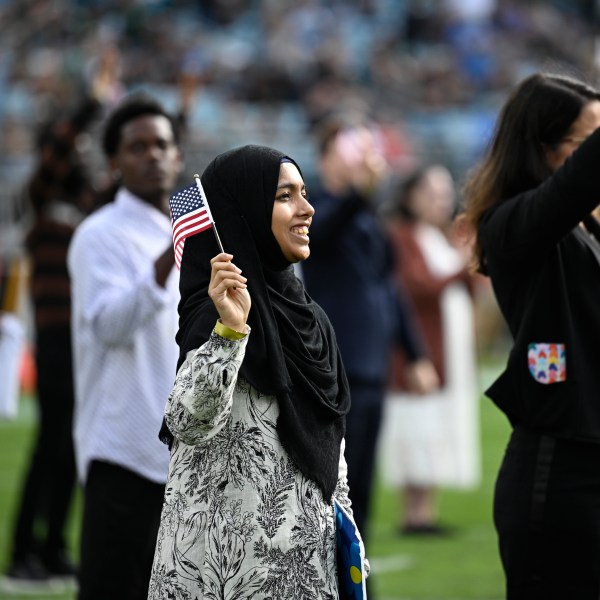 FILE - New United States citizens wave American flags during a naturalization ceremony during halftime at an NFL football game between the Jacksonville Jaguars and the New York Jets, Dec. 15, 2024, in Jacksonville, Fla. (AP Photo/Phelan M. Ebenhack, File)