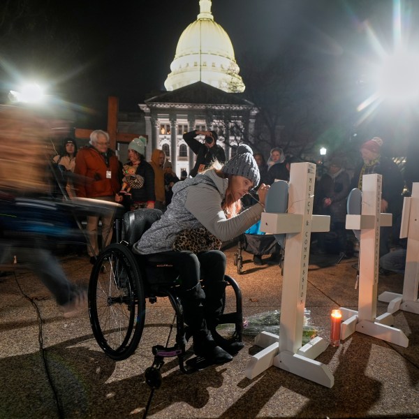 A supporter signs a cross during a candlelight vigil Tuesday, Dec. 17, 2024, outside the Wisconsin Capitol in Madison, Wis., following a shooting at the Abundant Life Christian School on Monday, Dec. 16. (AP Photo/Morry Gash)