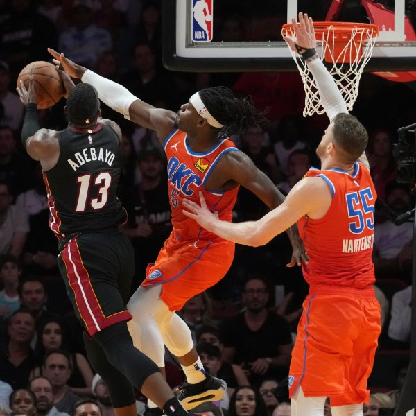 Oklahoma City Thunder guard Luguentz Dort (5) blocks a drive to the basket by Miami Heat center Bam Adebayo (13) during the first half of an NBA basketball game, Friday, Dec. 20, 2024, in Miami. (AP Photo/Marta Lavandier)