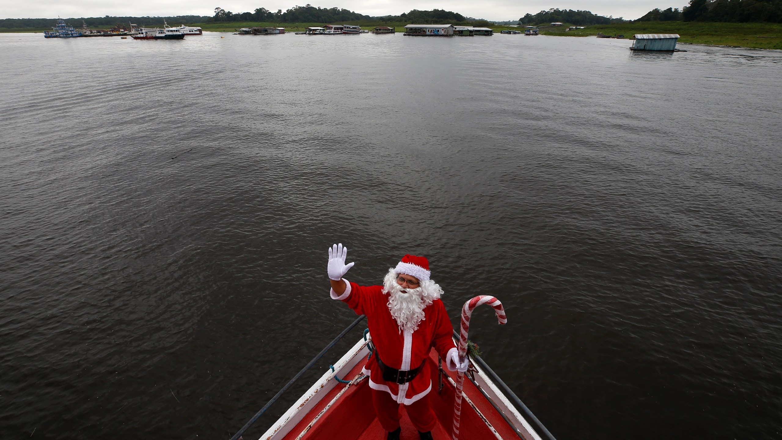 Jorge Barroso, dressed as Santa Claus, waves as he arrives on a boat to distribute Christmas gifts to children who live in the riverside communities of the Amazon, in Iranduba, Brazil, Saturday, Dec. 21, 2024. (AP Photo/Edmar Barros)