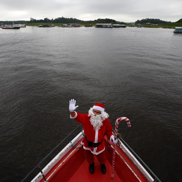 Jorge Barroso, dressed as Santa Claus, waves as he arrives on a boat to distribute Christmas gifts to children who live in the riverside communities of the Amazon, in Iranduba, Brazil, Saturday, Dec. 21, 2024. (AP Photo/Edmar Barros)