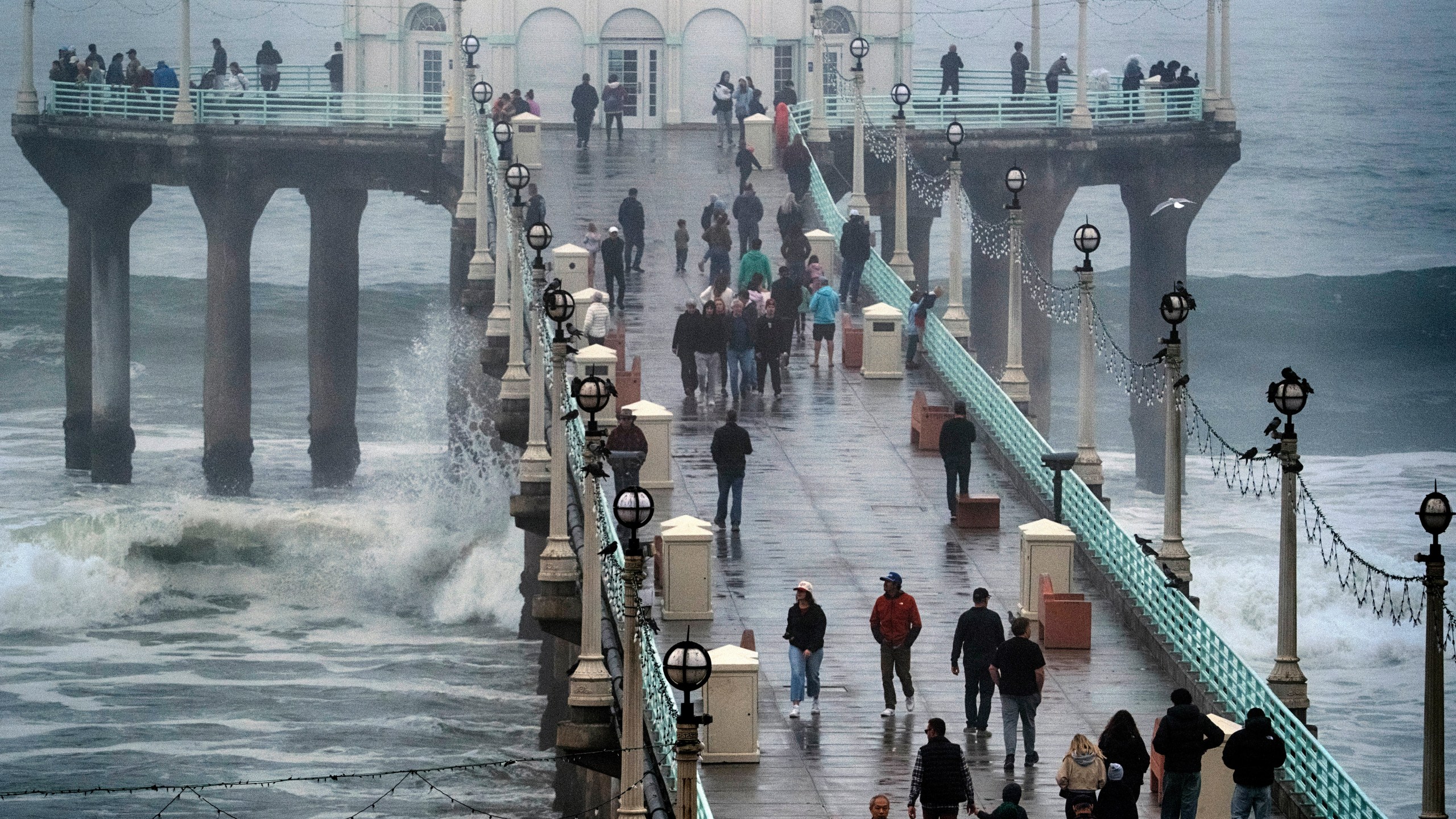 People brave the rain and walk along the Manhattan Beach Pier to watch high surf on Tuesday, Dec. 24, 2024 in Manhattan Beach, Calif. (AP Photo/Richard Vogel)