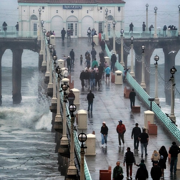 People brave the rain and walk along the Manhattan Beach Pier to watch high surf on Tuesday, Dec. 24, 2024 in Manhattan Beach, Calif. (AP Photo/Richard Vogel)