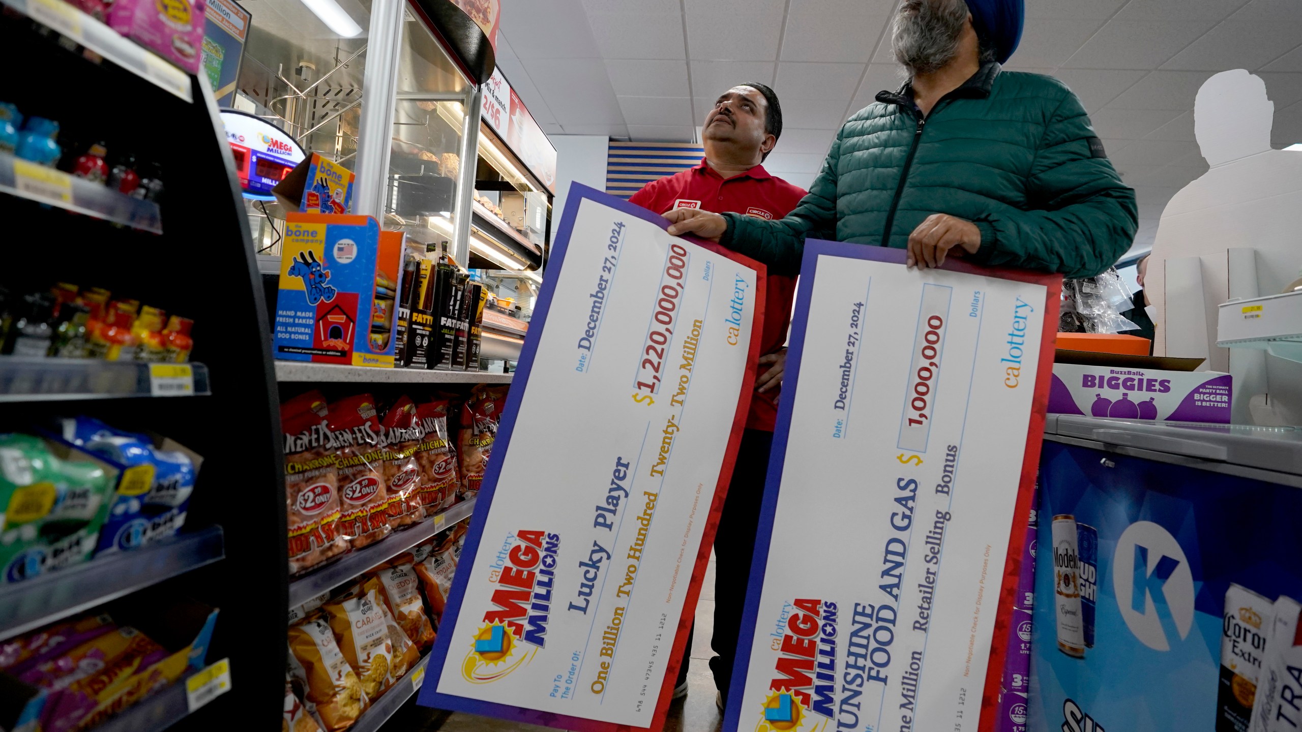 Jaspal Singh, right, and store employee Bob Singh, left, look for a spot to place two enlarged images of lottery payoff checks, at the family store, Saturday, Dec. 28, 2024, where the winning lotto ticket was purchased in Cottonwood, Calif. (AP Photo/Rich Pedroncelli).