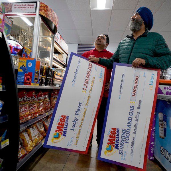 Jaspal Singh, right, and store employee Bob Singh, left, look for a spot to place two enlarged images of lottery payoff checks, at the family store, Saturday, Dec. 28, 2024, where the winning lotto ticket was purchased in Cottonwood, Calif. (AP Photo/Rich Pedroncelli).