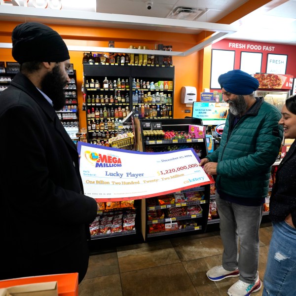 Ishar Gill, left, his father Jaspal Singh, center and his sister Jaspeet Gill right, look over the enlarged image of a check, Saturday, Dec. 28, 2024, that will be presented to the winner of $1.22 billion Mega Millions Lotto ticket that was purchased at their family's store in Cottonwood, Calif., Saturday, Dec. 28, 2024. (AP Photo/Rich Pedroncelli).