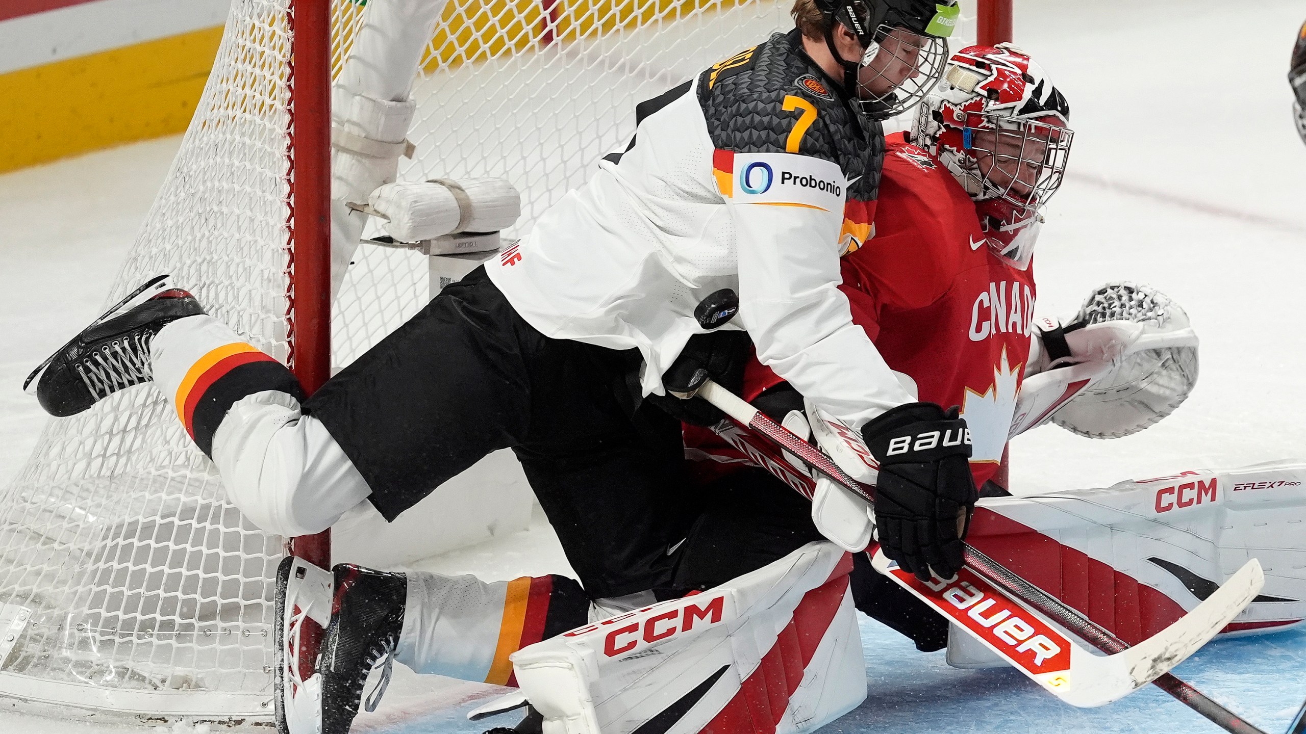 The puck hits Germany defenseman Carlos Handel (7) as he collides with Canada goaltender Carter George during first-period IIHF World Junior Hockey Championship tournament game action in Ottawa, Ontario, Sunday, Dec. 29, 2024. (Adrian Wyld/The Canadian Press via AP)