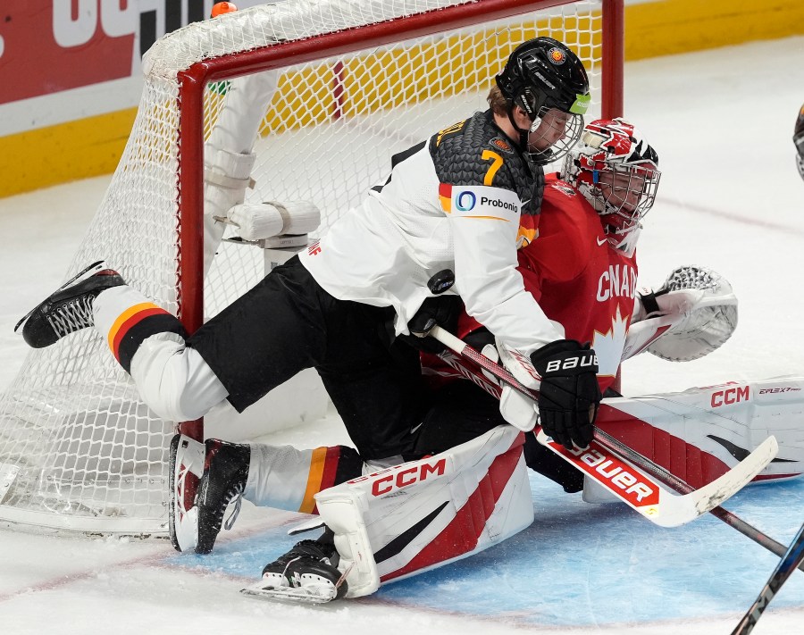 The puck hits Germany defenseman Carlos Handel (7) as he collides with Canada goaltender Carter George during first-period IIHF World Junior Hockey Championship tournament game action in Ottawa, Ontario, Sunday, Dec. 29, 2024. (Adrian Wyld/The Canadian Press via AP)