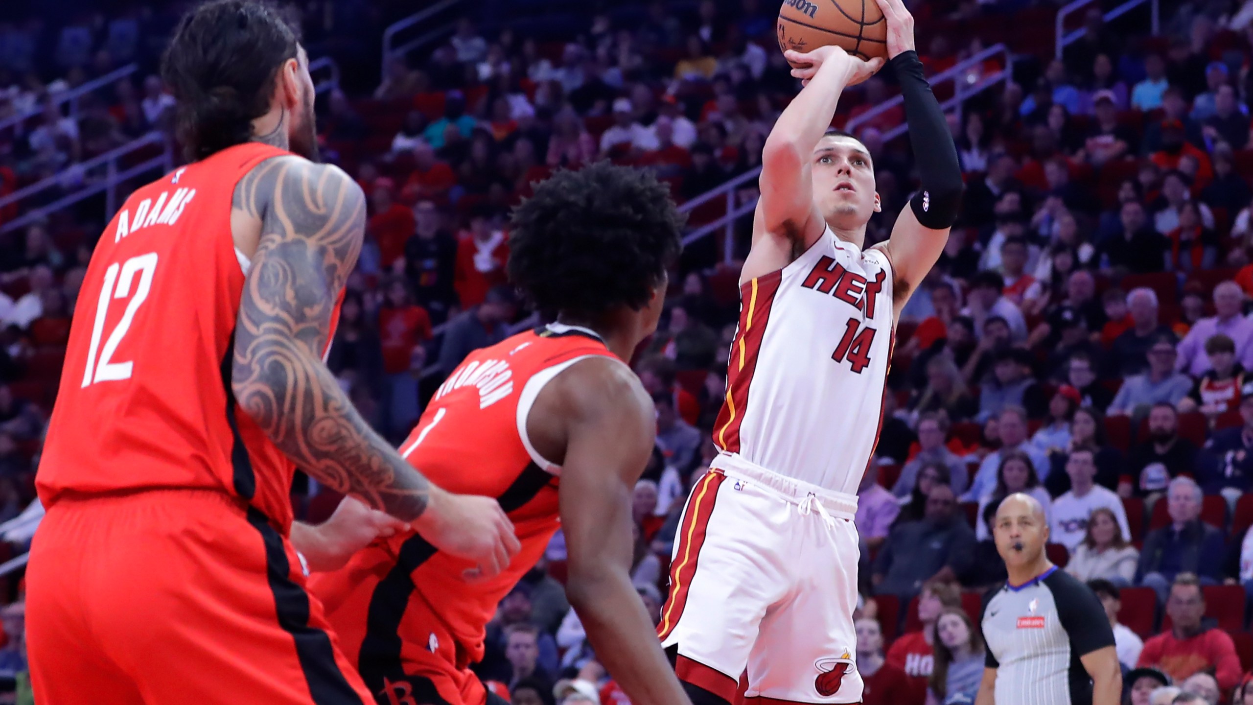 Miami Heat guard Tyler Herro (14) shoots a three-point shot as Houston Rockets center Steven Adams (12) and forward Amen Thompson, center, look on during the first half of an NBA basketball game Sunday, Dec. 29, 2024, in Houston. (AP Photo/Michael Wyke)