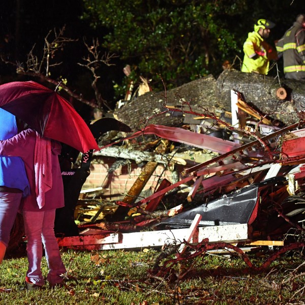 Bystanders hug as first responders work to free a victim after a tree fell on a house in Natchez, Miss., Saturday, Dec. 28, 2024. (Thomas Graning/The Natchez Democrat via AP)