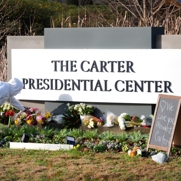 Christine Mason, of Atlanta, places flowers at entrance the The Jimmy Carter Presidential Center in Atlanta Monday, Dec. 30, 2024, in Atlanta. Formr President Jimmy Carter died Sunday at his home in Plains, Ga, at the age of 100. (AP Photo/John Bazemore )