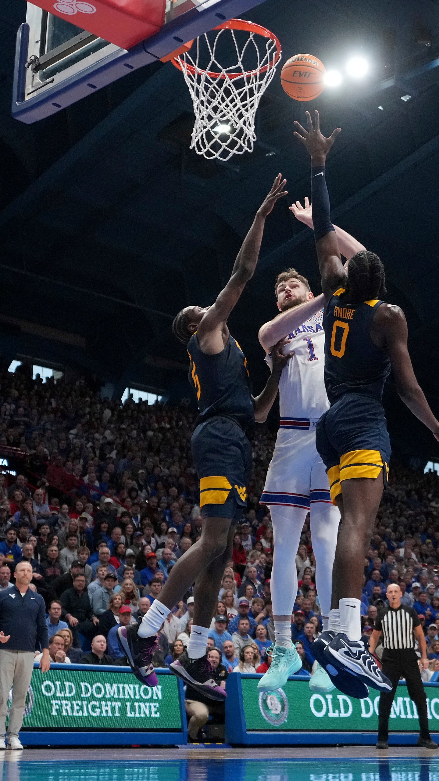 Kansas center Hunter Dickinson (1) shoots between West Virginia guard Toby Okani, left, and center Eduardo Andre (0) during the first half of an NCAA college basketball game, Tuesday, Dec. 31, 2024, in Lawrence, Kan. (AP Photo/Charlie Riedel)