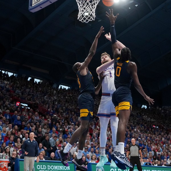 Kansas center Hunter Dickinson (1) shoots between West Virginia guard Toby Okani, left, and center Eduardo Andre (0) during the first half of an NCAA college basketball game, Tuesday, Dec. 31, 2024, in Lawrence, Kan. (AP Photo/Charlie Riedel)