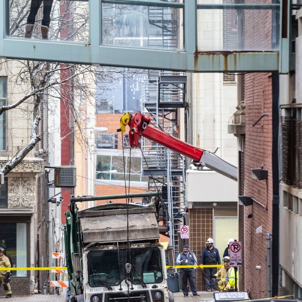 A person watches from a skywalk as workers use a crane to lift a garbage truck that got stuck in a sinkhole in downtown Omaha, Neb., Thursday, Jan. 2, 2025. (Chris Machian/Omaha World-Herald via AP)