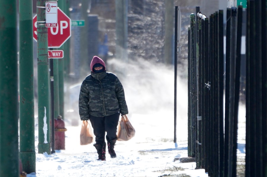 FILE - A person walk almost a half mile to their home from a grocery store as steam from an underground vent rises behind them in the Bronzeville neighborhood of Chicago, Tuesday, Jan. 16, 2024. (AP Photo/Charles Rex Arbogast, File)