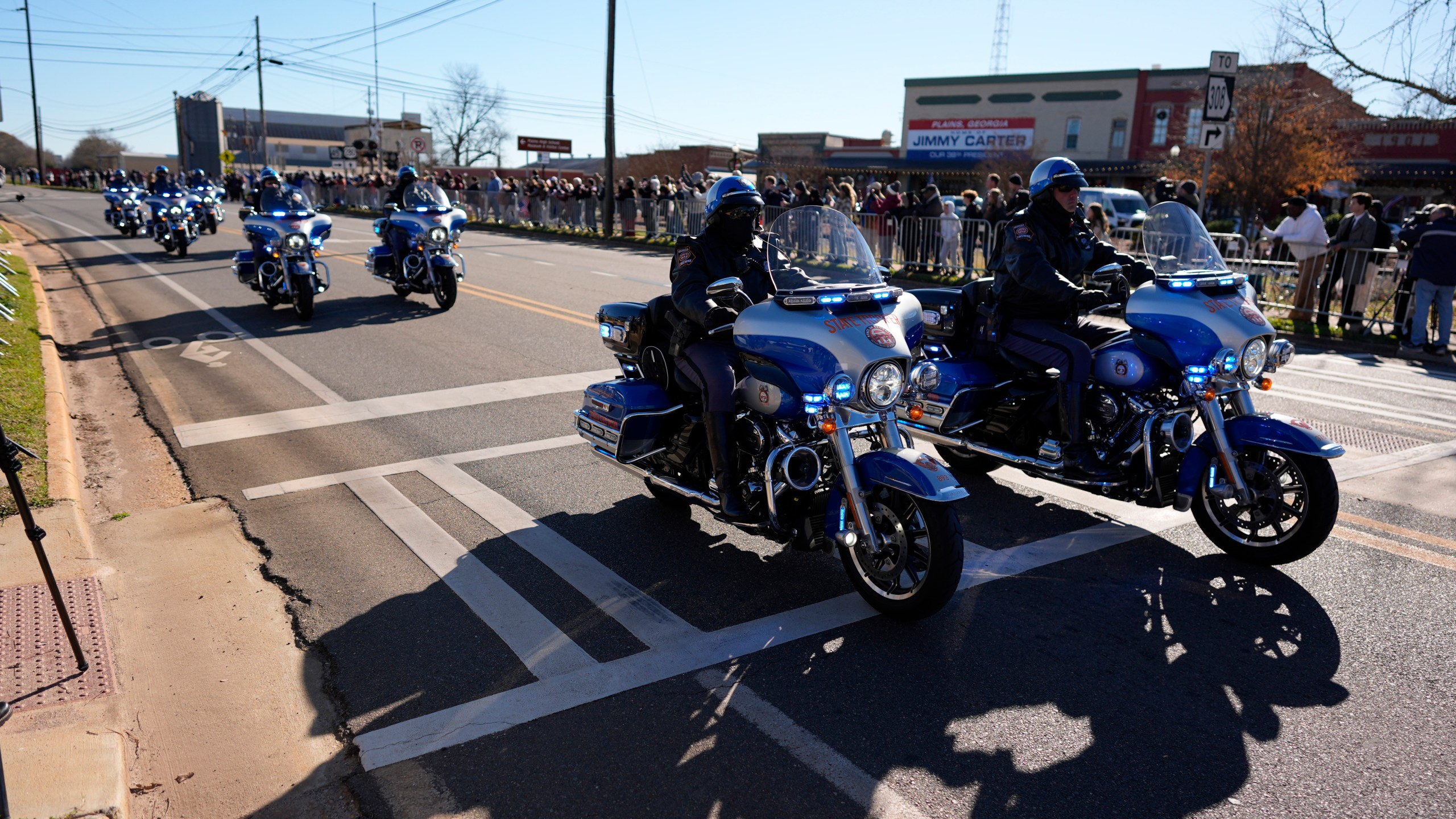 A police escort passes as the hearse carrying the flag-draped casket of former President Jimmy Carter approaches during a procession in downtown Plains, Ga., Saturday, Jan. 4, 2025. (AP Photo/Mike Stewart)