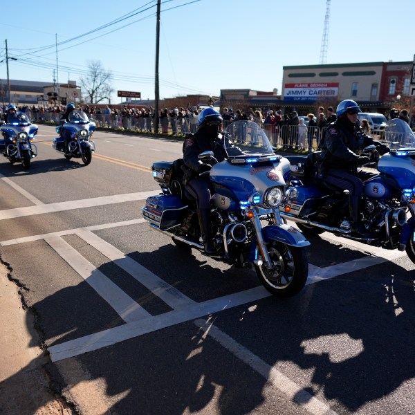 A police escort passes as the hearse carrying the flag-draped casket of former President Jimmy Carter approaches during a procession in downtown Plains, Ga., Saturday, Jan. 4, 2025. (AP Photo/Mike Stewart)