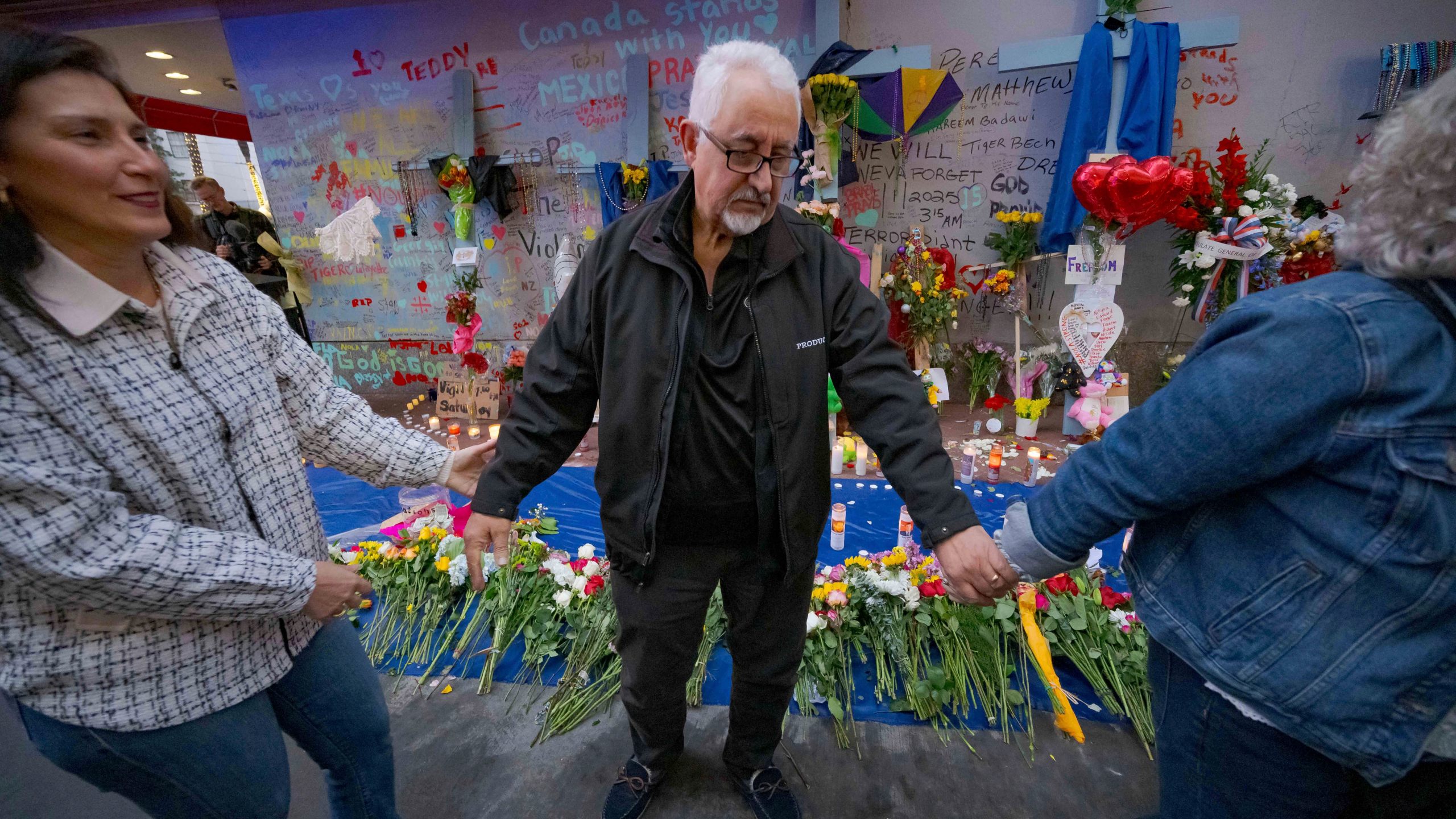 Long Island, New York residents Louis Tenedorio holds hands with family friend Angelique Whittington, left, and his wife, Cathy Tenedorio, by a memorial on Bourbon Street and Canal Street in New Orleans, Saturday, Jan. 4, 2025, where his son, Matthew Tenedorio, was killed as one of the victims of the New Year's Day deadly truck attack and shooting. (AP Photo/Matthew Hinton)