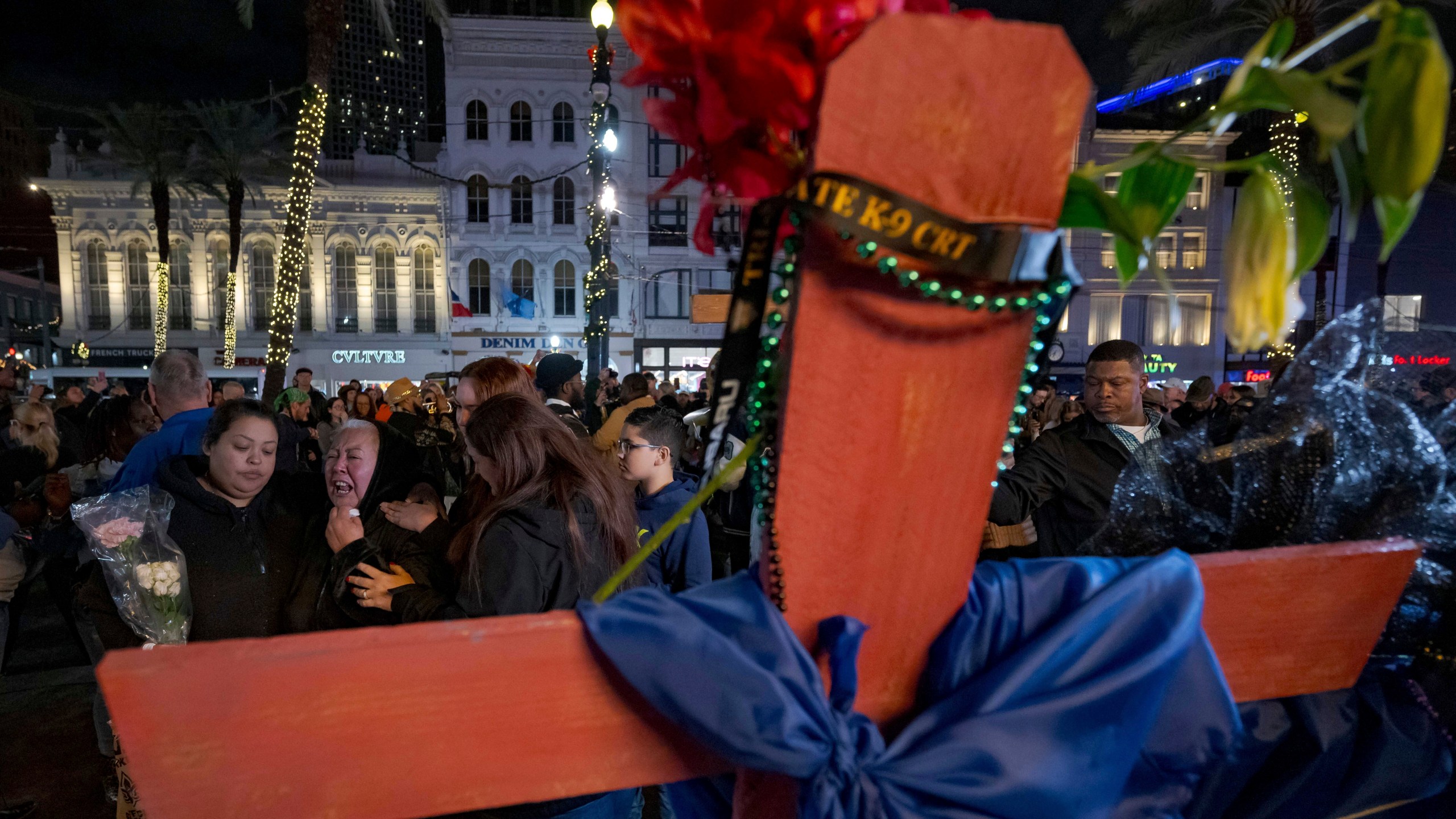 Jessica Perez, holding flowers left, hugs her mother Martha Perez who cries out by a cross memorializing her daughter, Nicole Perez, who was a victim on the New Year's Day attack, on Canal Street near the intersection of Bourbon Street in New Orleans, Saturday, Jan. 4, 2025. (AP Photo/Matthew Hinton)