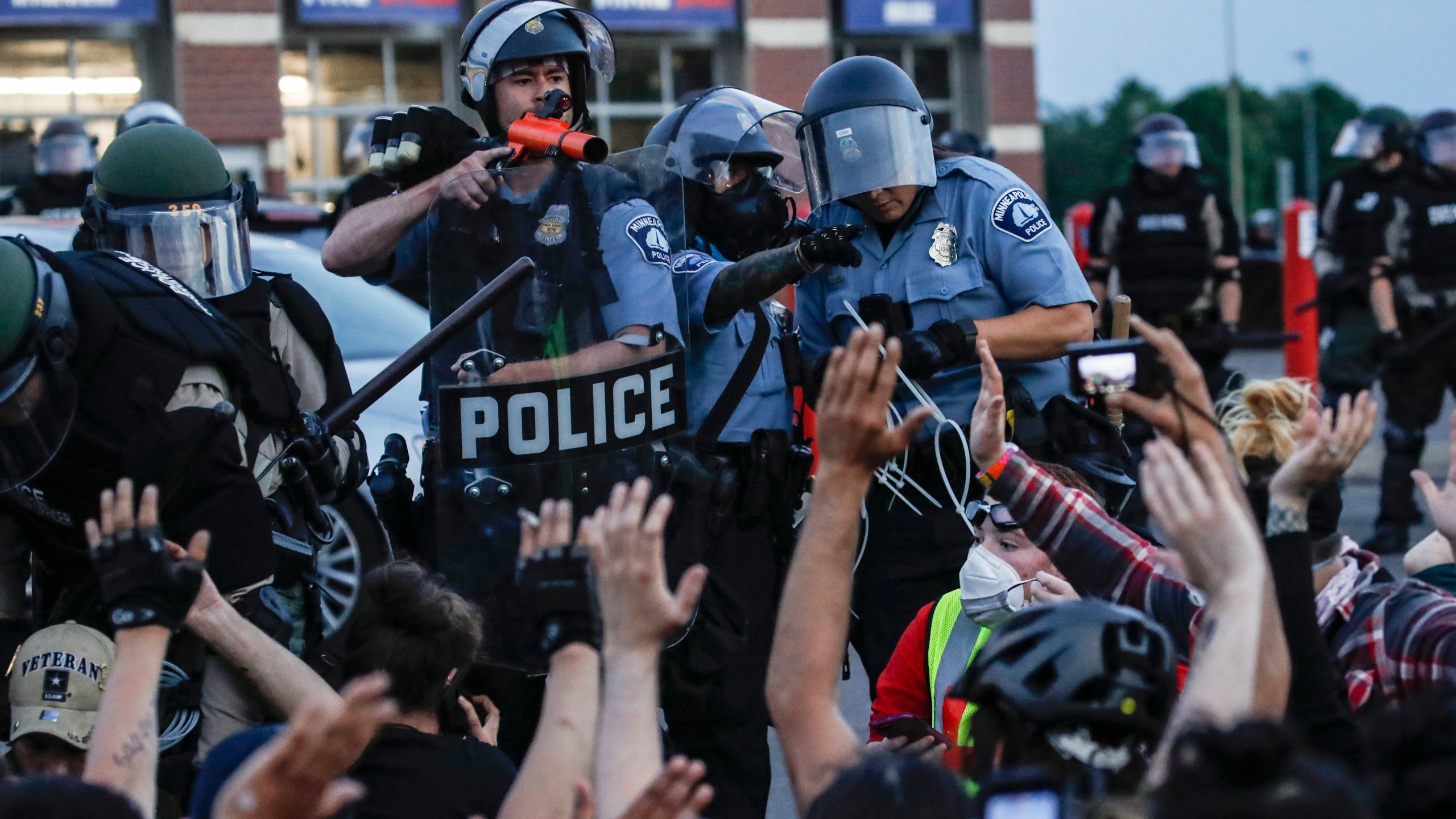 FILE - A police officer points a hand cannon at protesters who have been detained pending arrest on South Washington Street in Minneapolis, May 31, 2020, as protests continued following the death of George Floyd. (AP Photo/John Minchillo, File)