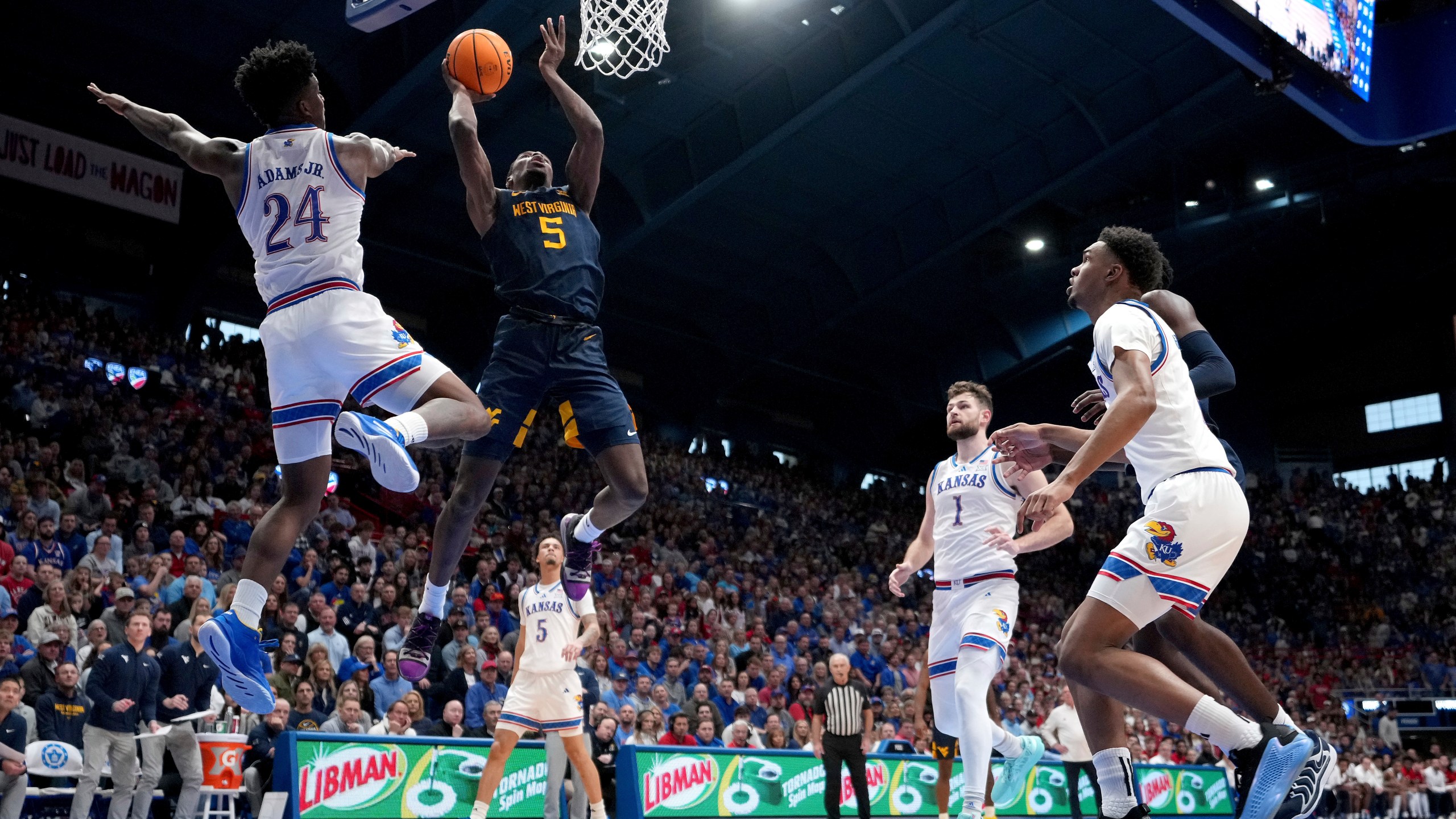 West Virginia guard Toby Okani (5) gets past Kansas forward KJ Adams Jr. (24) to put up a shot during the second half of an NCAA college basketball game, Tuesday, Dec. 31, 2024, in Lawrence, Kan. West Virginia won 62-61(AP Photo/Charlie Riedel)