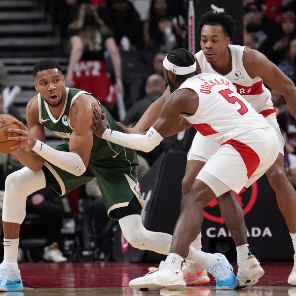 Milwaukee Bucks forward Giannis Antetokounmpo, left, looks to pass the ball while under pressure from Toronto Raptors guard Immanuel Quickley (5) and Scottie Barnes, right, during first-half NBA basketball game action in Toronto, Monday, Jan. 6, 2025. (Nathan Denette/The Canadian Press via AP)