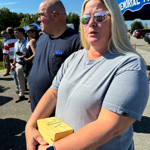 Shannon Doughty stands in front of her husband, Matt, while holding a wooden box on Aug. 29, 2024, in Westfield, Indiana, that had contained some of the cremated remains of her late brother Allen Livingston, who was identified in October 2023 as the ninth known victim of suspected serial killer Herbert Baumeister. (AP Photo/Rick Callahan)