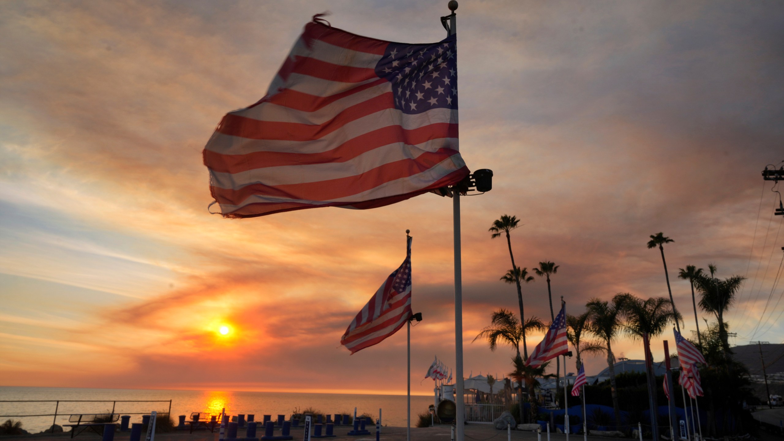 FILE - Flags fly under heavy winds before sunset as a plume of smoke from the Franklin Fire rises over the ocean Tuesday, Dec. 10, 2024, in Malibu, Calif. (AP Photo/Damian Dovarganes,File)