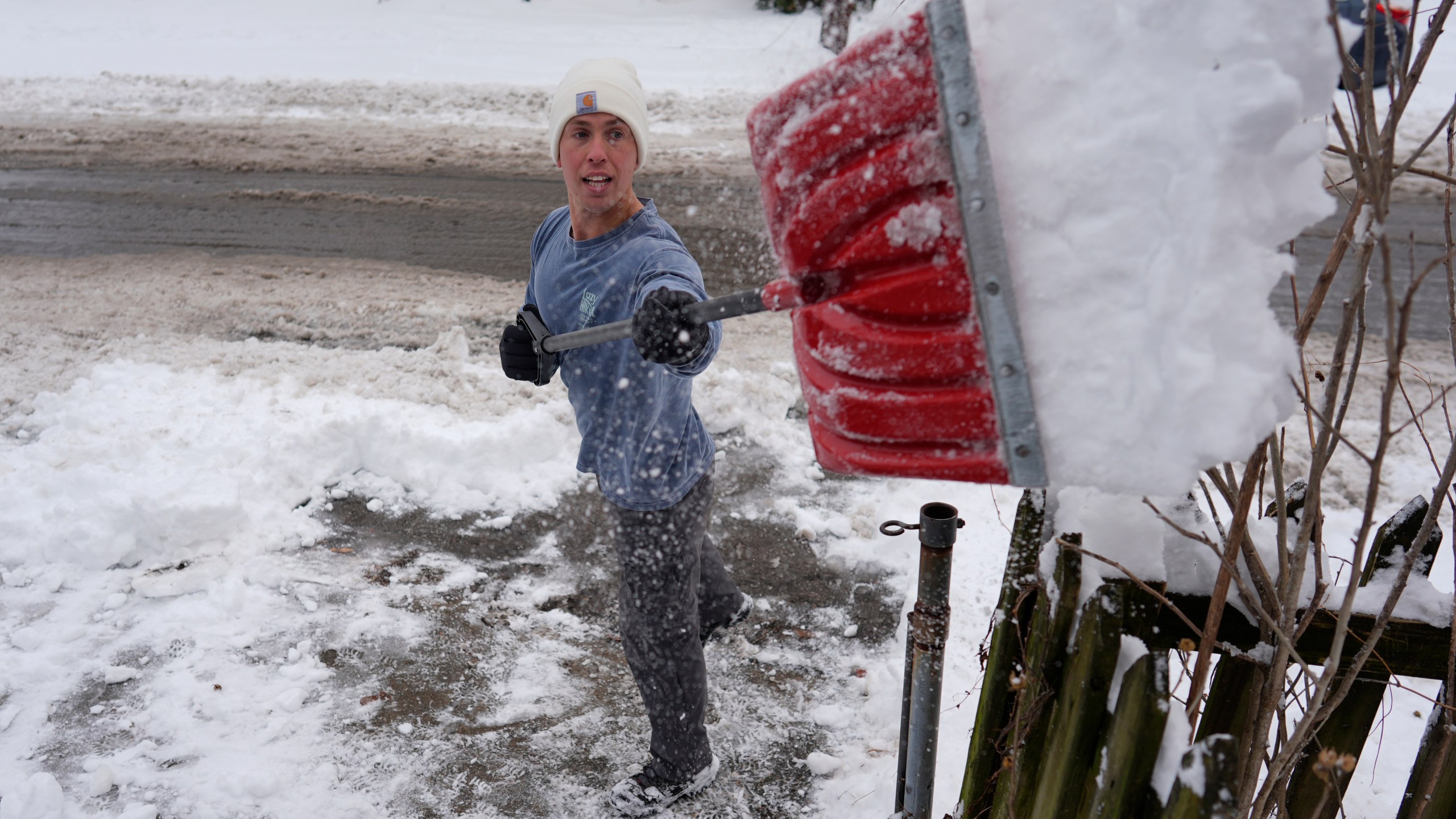 Ben Sisarsky pitches snow over a fence as he clears his girlfriend's parking spot with a borrowed snow shovel in Cincinnati, Tuesday, Jan. 7, 2025. (AP Photo/Carolyn Kaster)