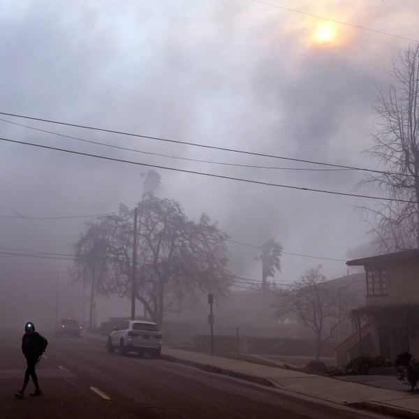 A pedestrian uses a flashlight to make his way down a smoke-filled street during wildfires in the Altadena section of Pasadena, Calif., Wednesday, Jan. 8, 2025. (AP Photo/Chris Pizzello)