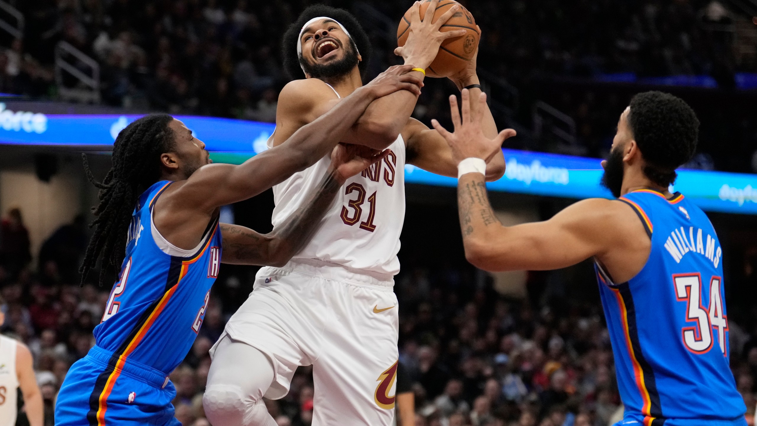 Cleveland Cavaliers center Jarrett Allen (31) is fouled by Oklahoma City Thunder guard Cason Wallace, left, as he drives to the basket between Wallace and Kenrich Williams (34), right, in the first half of an NBA basketball game, Wednesday, Jan. 8, 2025, in Cleveland. (AP Photo/Sue Ogrocki)