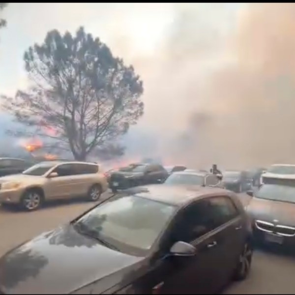 CORRECTS LOCATION TO PACIFIC PALISADES, INSTEAD OF GLENHAVEN - People evacuate their cars as flames from a wildfire spread to the street near Pacific Palisades, Calif., on Tuesday, Jan. 7, 2025. (Aaron Samson via AP)